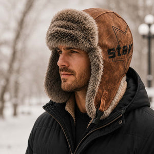Brown men’s winter trapper hat with faux-fur ear flaps worn with a black winter jacket.