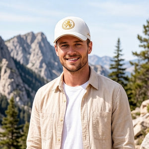 White embroidered cotton baseball cap with gold front emblem, curved brim, and adjustable unisex fit